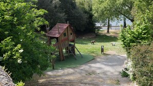 Une maison de jeu en bois avec un toit rouge, une zone herbeuse et un escalier en pierre menant à l’étage.