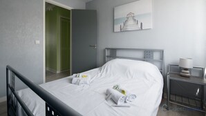 Une chambre d’hôtel avec un lit, une table de chevet avec une lampe, une porte verte et un tableau au mur.