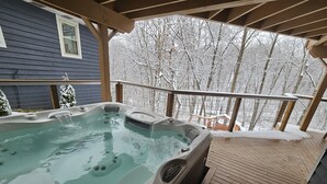 A hot tub on a wooden deck with a view of snow-covered trees.