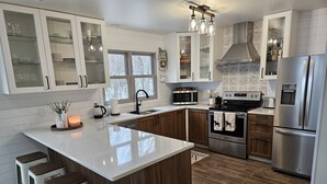 A modern kitchen with a large island, stainless steel appliances, wooden cabinets, and a window overlooking the outdoors.