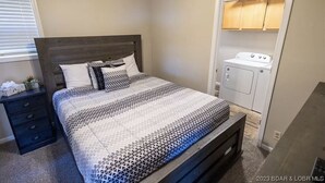 A bedroom with a bed, a nightstand, a dresser, and a built-in washer and dryer.