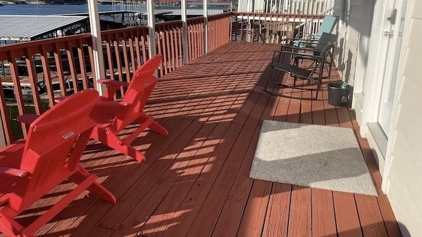 A wooden deck with red Adirondack chairs, a white door, and a view of a lake and buildings in the background.