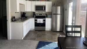 A compact kitchen with white cabinets, a stainless steel refrigerator, a microwave, and a stove.