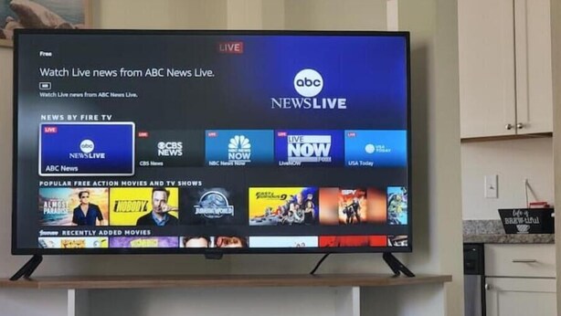 Een flatscreen televisie toont een interface van een nieuwskanaal met diverse nieuwskanalen en een sectie voor gratis actiefilms en tv-series.