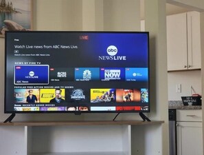 Una televisió de pantalla plana mostra una interfície de cadena d'informatius amb diverses cadenes d'actualitat i una secció per a pel·lícules d'acció i sèries de televisió gratuïtes.