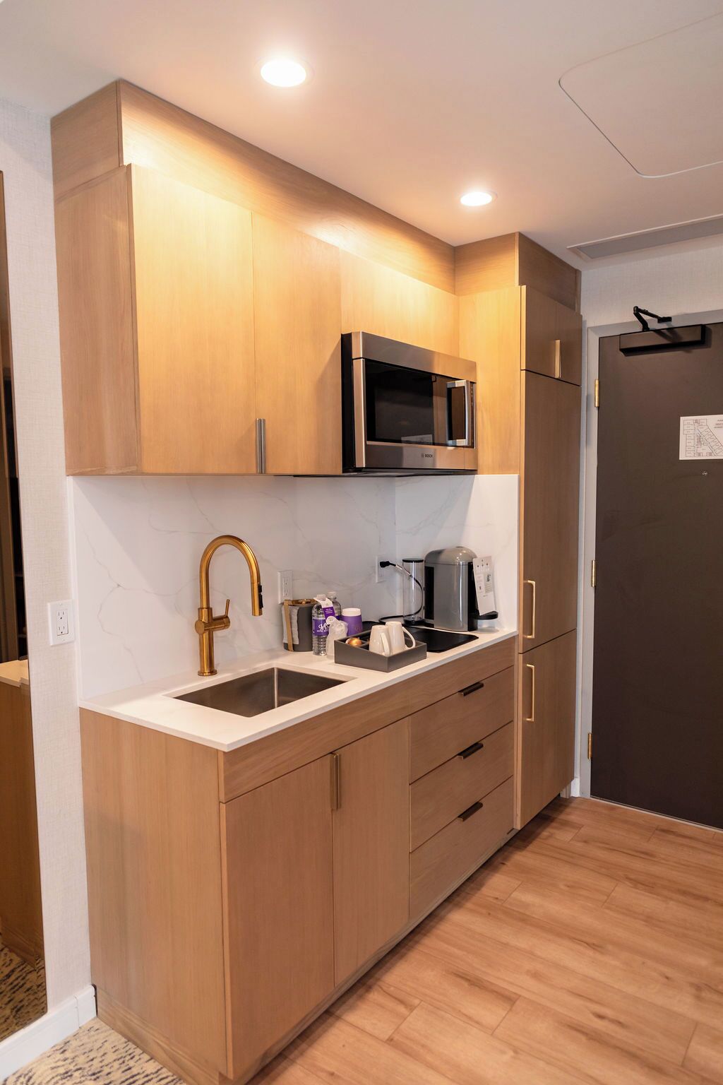 A modern kitchen with wooden cabinets, a stainless steel microwave, a coffee maker, and a sink.