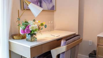 A modern study room with a white desk, a gold lamp, a vase with flowers, and a large abstract painting on the wall.