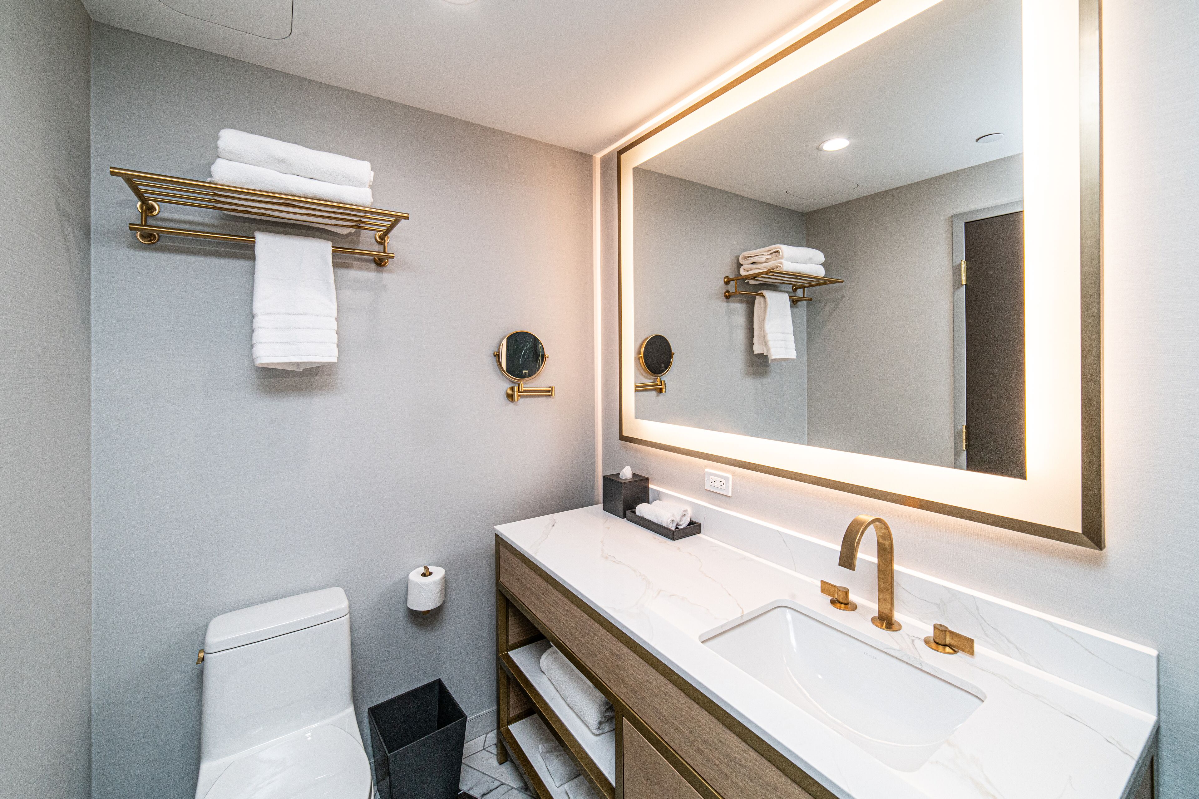 Ein modernes Badezimmer mit einem weißen Waschbecken, goldenen Armaturen und einem großen Spiegel.