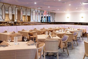 A restaurant with round tables and cushioned booths, featuring a marble wall and ceiling with reflective panels. - Iris Hotel Boston (Brookline)