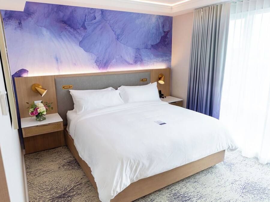 A hotel room with a large bed, a nightstand with a lamp, and a wall-mounted artwork.