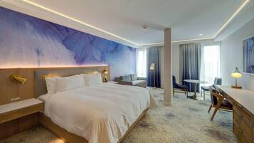 A modern hotel room with a large bed, a desk, and a seating area.