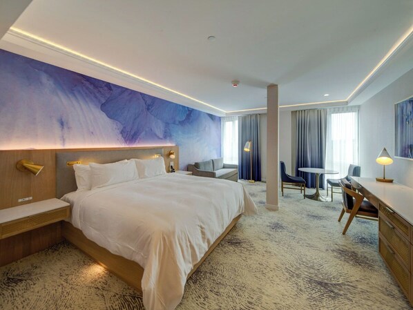 Habitación de hotel moderna con una cama grande, un escritorio y una zona de estar.