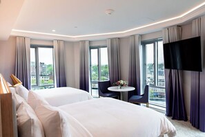 A hotel room with two beds, a round table with chairs, a TV, and large windows with curtains. - Iris Hotel Boston (Brookline)