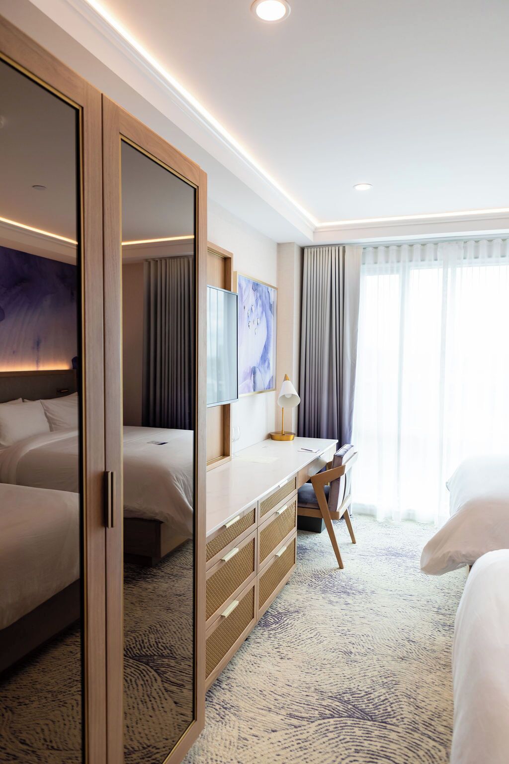Habitación de hotel con una cama grande, un escritorio con silla, un armario y un espejo amplio.