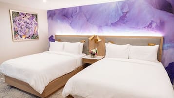 Een hotelkamer met twee bedden, een groot abstract schilderij aan de muur, en een klein tafeltje met een lamp en bloemen.