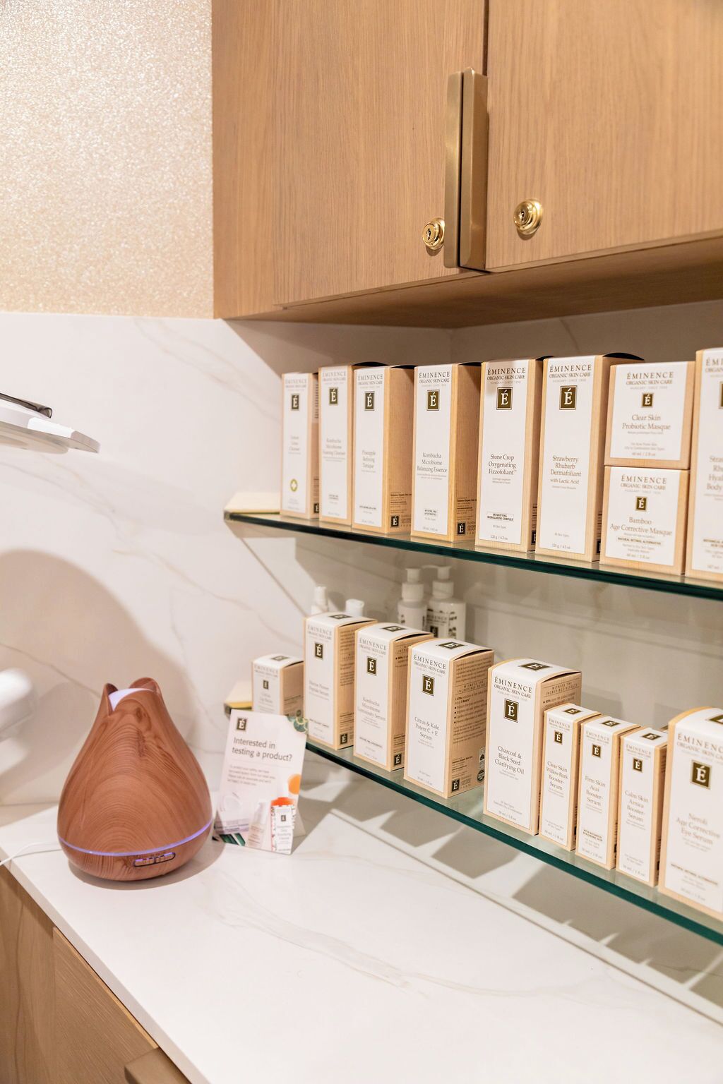 A shelf with various skincare products, a wooden cabinet above, and a white marble countertop.