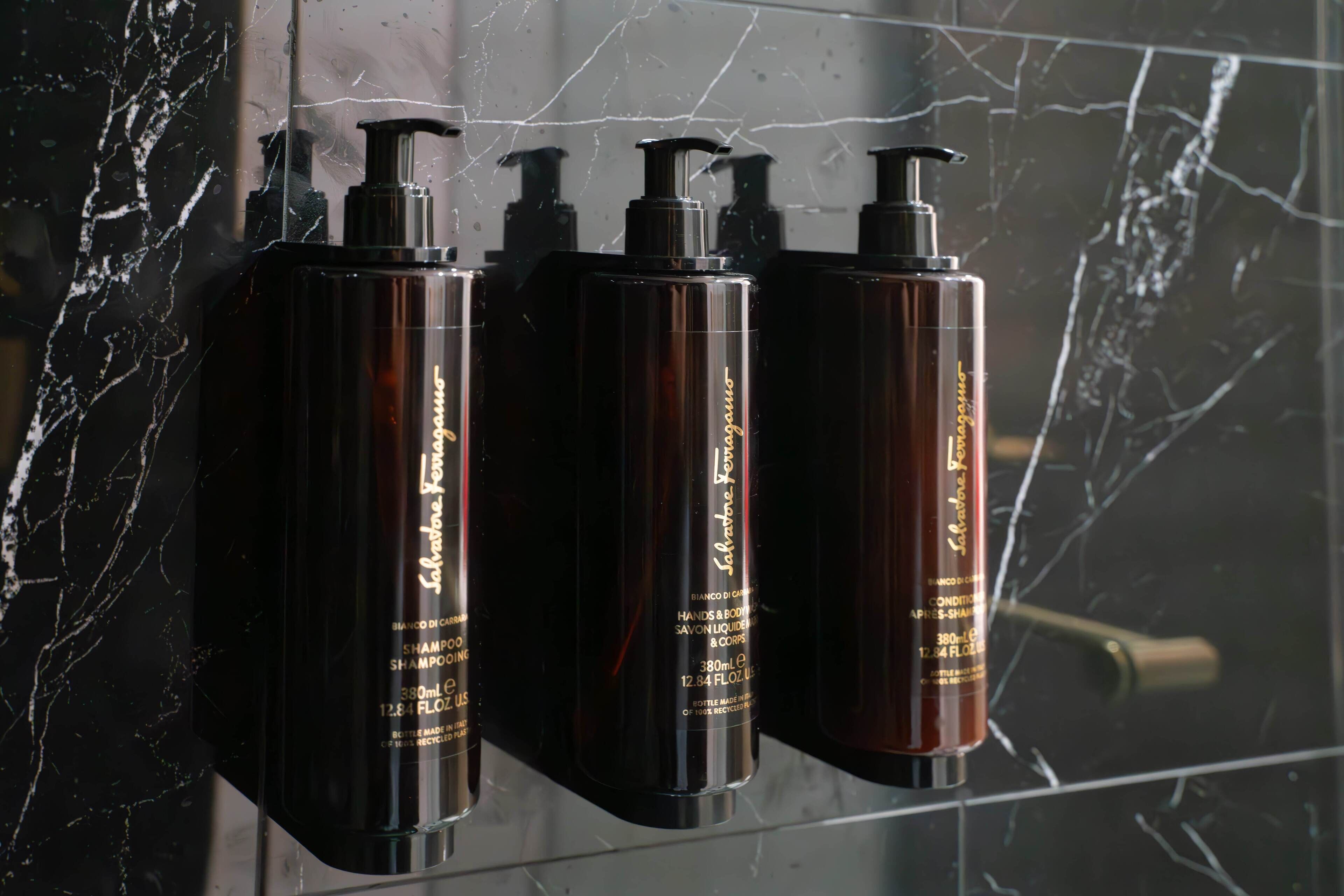 Tres botellas negras con letras doradas sobre una pared de mármol.