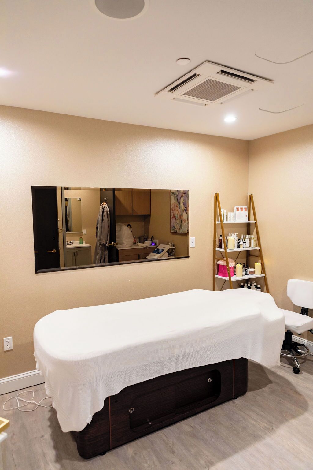 A room with a large mirror, a massage table, a shelf with bottles, and a ladder.