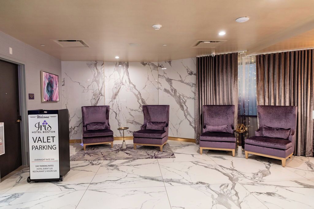 Eine Hotellobby mit Marmorböden, violetten Sesseln, einem Schild für den Valet-Parkservice und einem modernen Deckenstil.