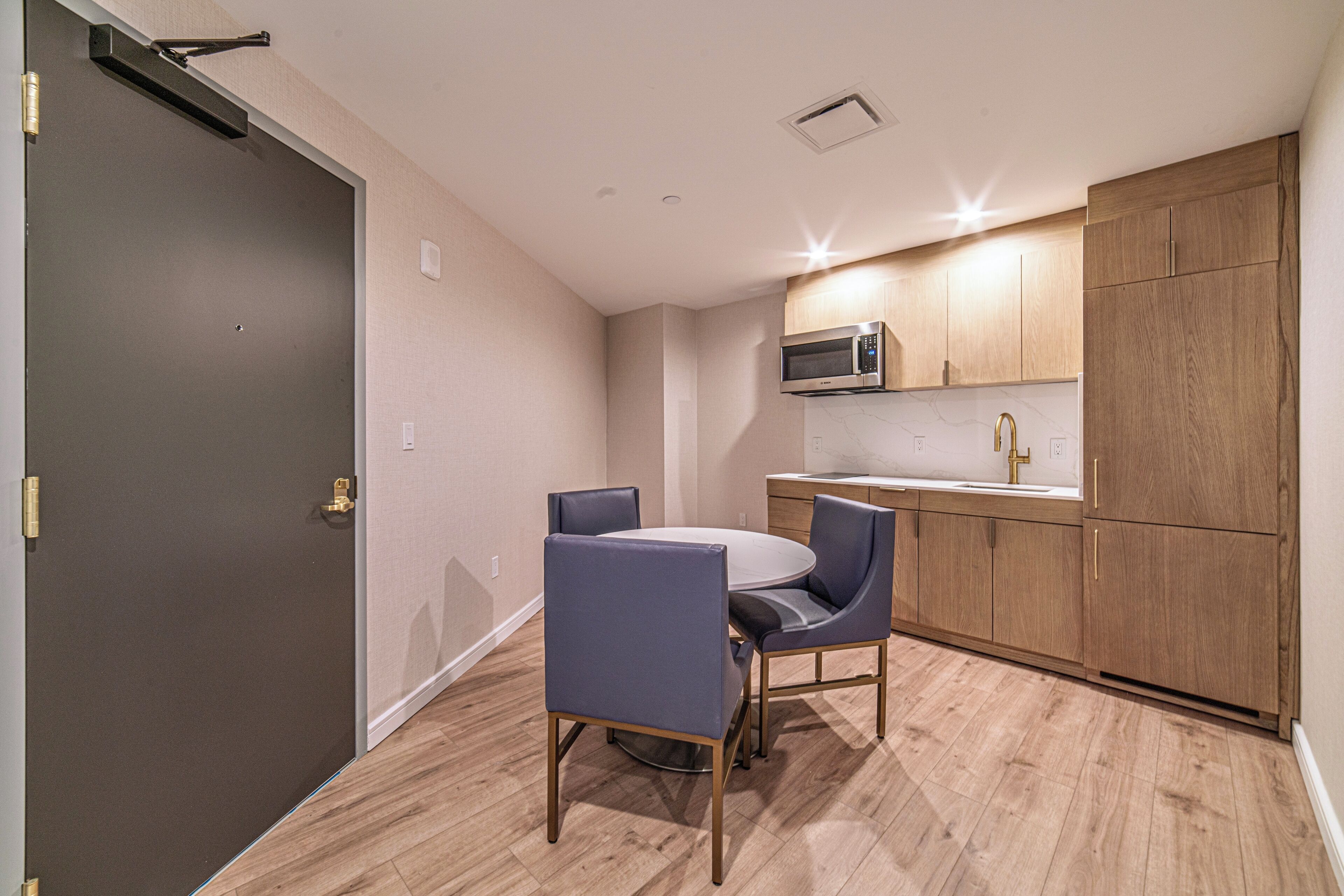 A compact kitchen with a microwave, wooden cabinets, and a dining area with two chairs.