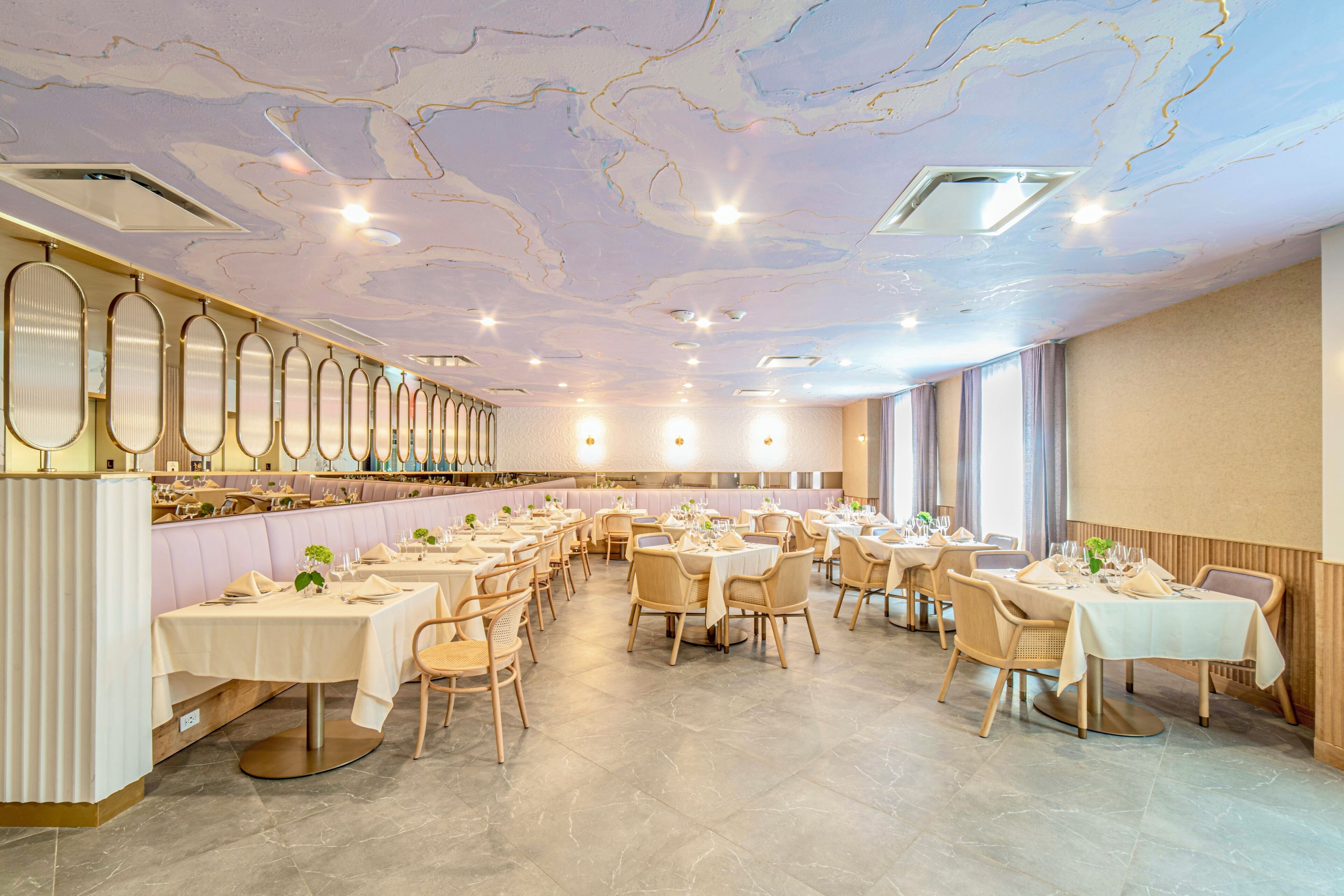 A spacious dining area with multiple tables and chairs, a long counter with a bar, and a ceiling with a marble-like design.