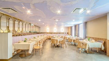 A spacious dining area with multiple tables and chairs, a long counter with a bar, and a ceiling with a marble-like design.