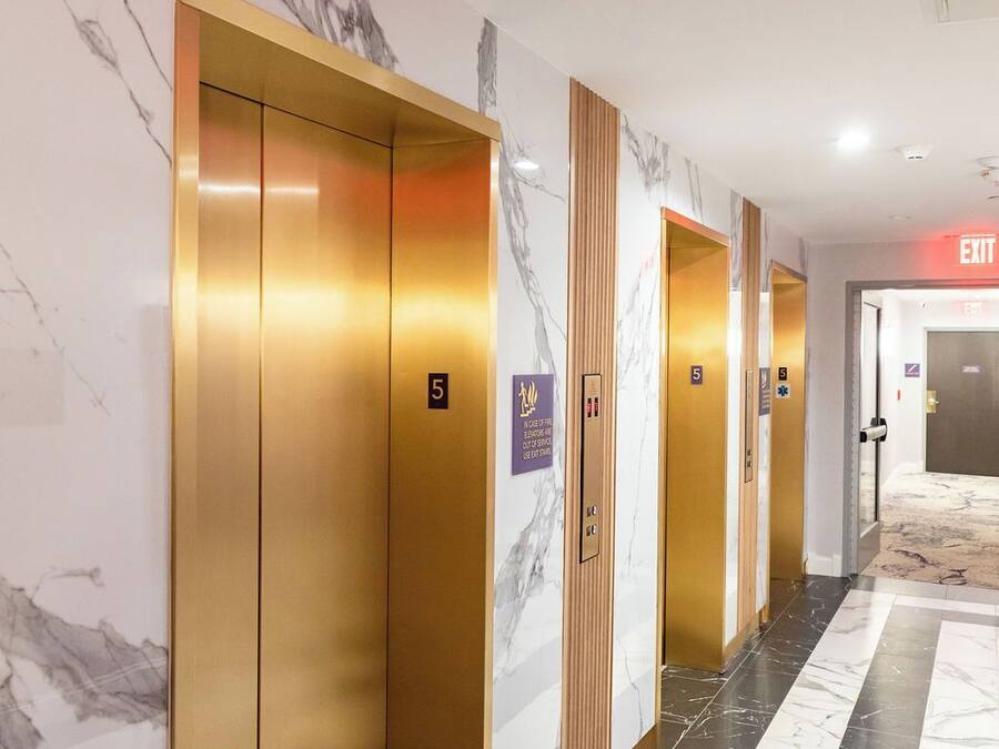 A hallway with marble walls and floors, featuring elevators and an exit sign.