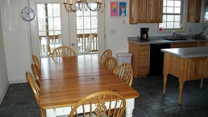 Una cocina con armarios de madera, una mesa de comedor, sillas, una araña y vistas por la puerta.