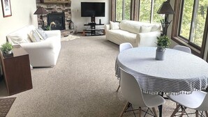 A spacious living room with a stone fireplace, a flat-screen TV, and a dining area with a table and chairs. - Lovely Views - Top of the Mountain - Foosball & Pool Table - Screened in Porch (McGaheysville)