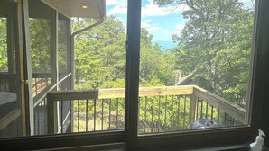 A covered outdoor area with a wooden deck and railing, overlooking a forested landscape. - Lovely Views - Top of the Mountain - Foosball & Pool Table - Screened in Porch (McGaheysville)