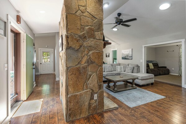 Un salón amplio con una pared decorativa de piedra, un ventilador de techo y un conjunto de sofás.