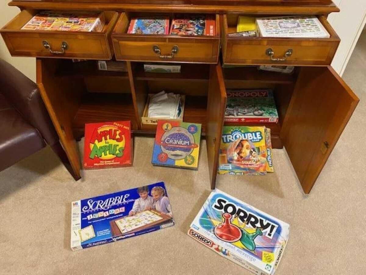 A wooden desk with multiple drawers and shelves, holding various board games and a Scrabble game on the floor.