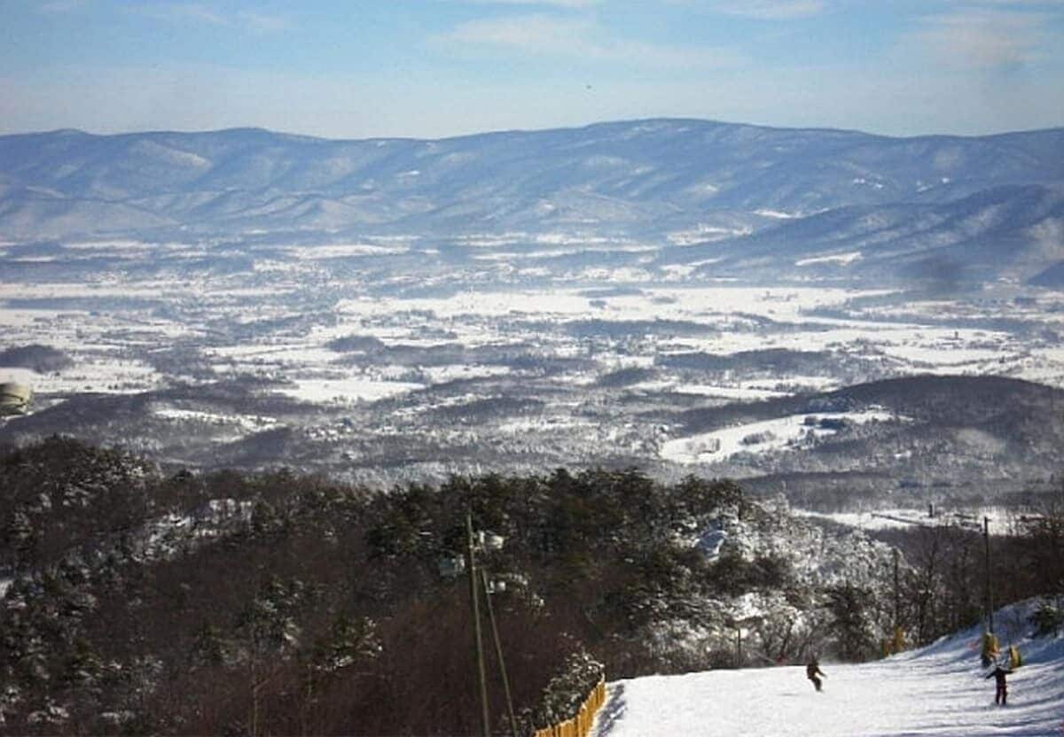 A snowy landscape with a ski slope, trees, and distant mountains.