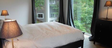 A bedroom with a bed, two bedside lamps, a dresser, and a window with curtains.