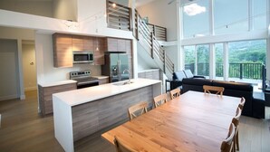 A modern kitchen with a central island, a dining area with a wooden table, and a staircase leading to a loft. - Stunning Views and Tastefully Decorated; Middle of Mtn; Work Space; Games & WiFi (McGaheysville)