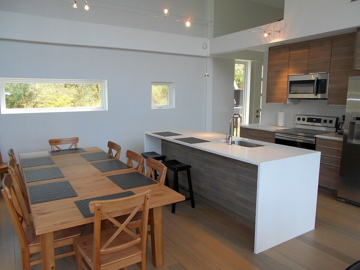 A modern kitchen with a central island, wooden dining table, and built-in appliances.