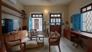 Uma sala de estar acolhedora com móveis de madeira, TV e uma área de cozinha com armários azuis e uma janela.