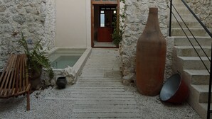 Um pátio de paredes de pedra com um banco de madeira, um vaso de terracota grande e uma escadaria que leva a uma porta.