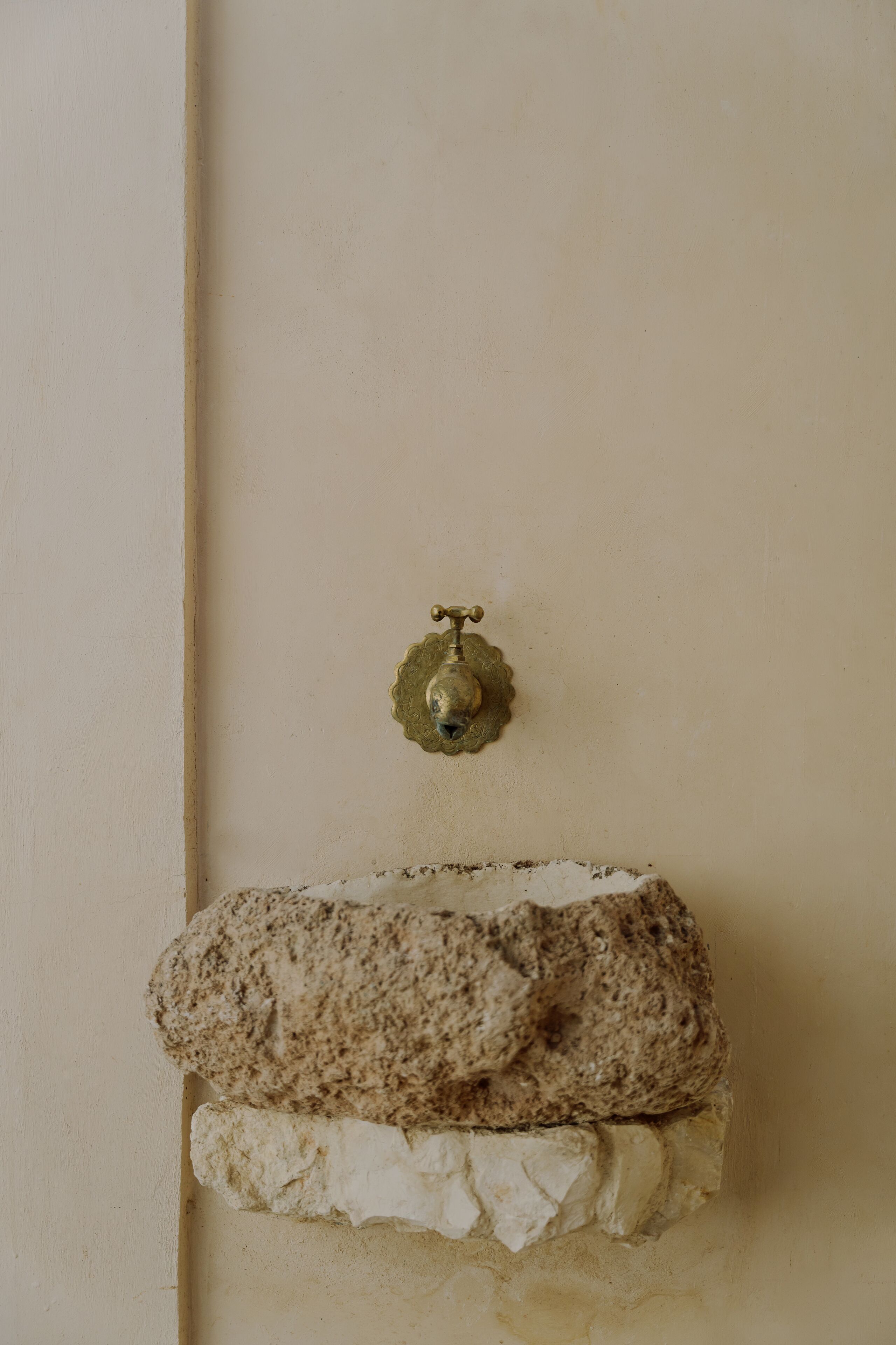 A wall-mounted brass faucet with a decorative base, a textured stone-like surface, and a rough, white stone base.