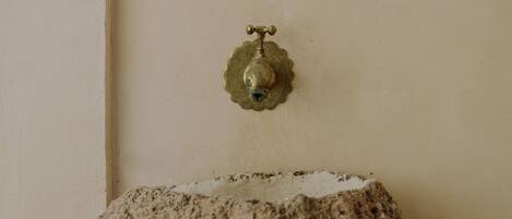 A wall-mounted brass faucet with a decorative base, a textured stone-like surface, and a rough, white stone base.