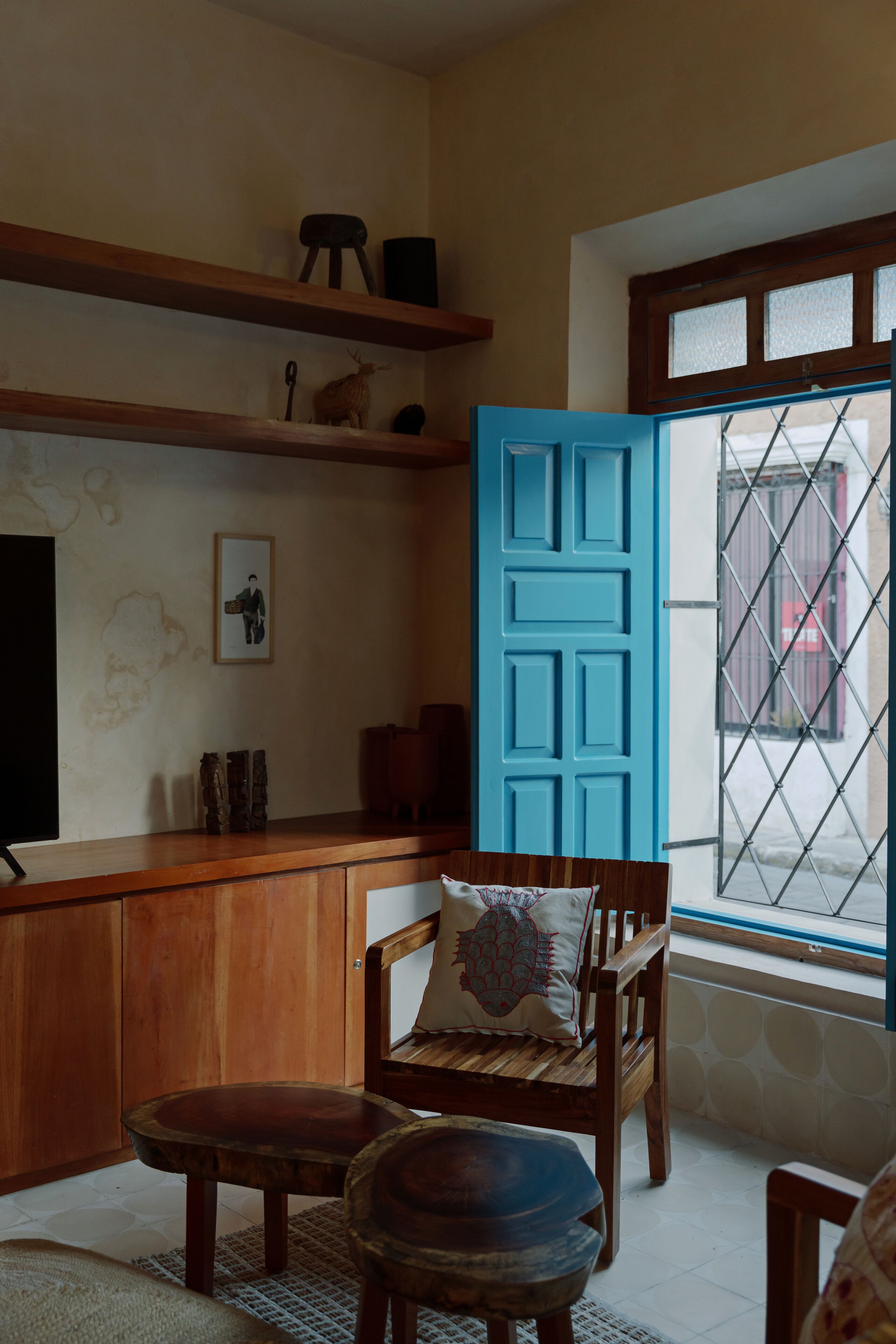 A room with a wooden desk, a blue door, and a window with a view of a gate.
