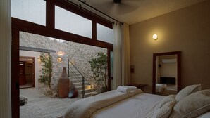 Quarto com cama grande, parede de pedra e vista para o exterior.