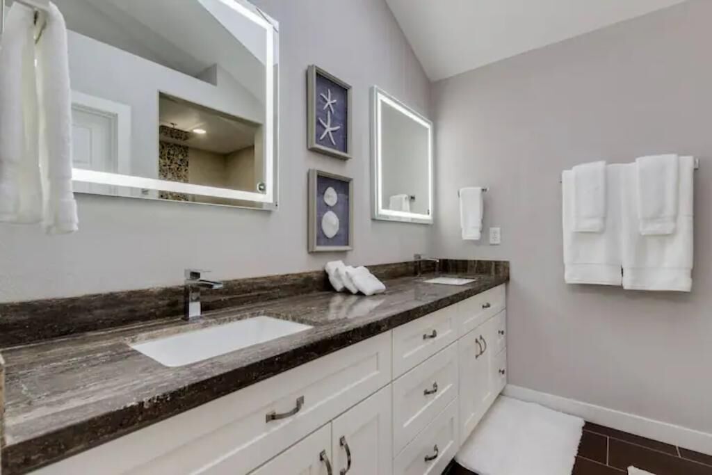 A modern bathroom with a large mirror, two sinks, and a vanity with drawers.