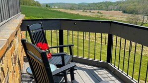 Un balcon donnant sur un champ verdoyant et des collines.