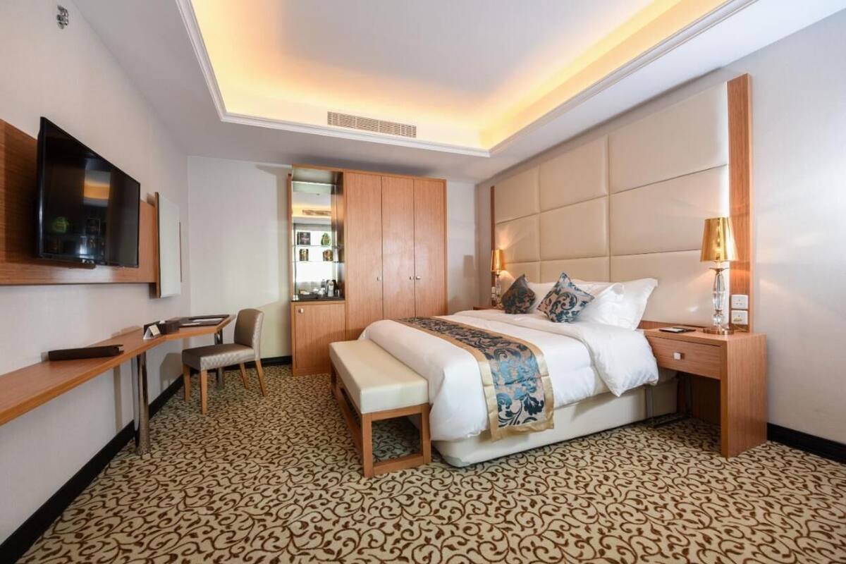 A hotel room with a large bed, a desk, a chair, a TV, and a wardrobe.