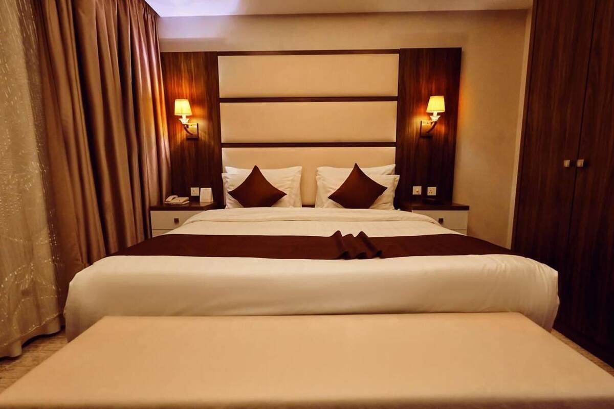 A hotel room with a large bed, two bedside tables, two wall-mounted lamps, and a curtain.