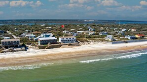 Vue aérienne d’une zone résidentielle côtière, avec des maisons, une plage et une étendue d’eau en arrière-plan.
