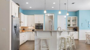 Una cocina moderna con armarios blancos, una isla central con taburetes y un refrigerador de acero inoxidable.