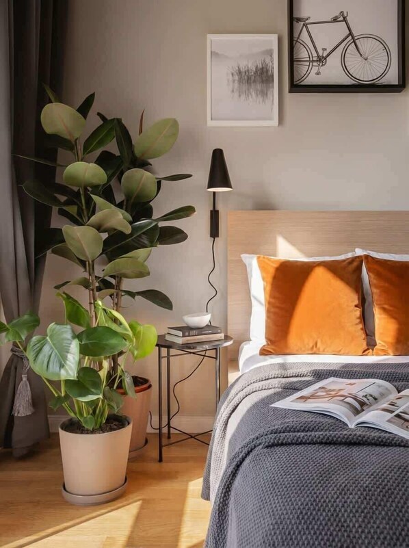 A neatly arranged bedroom with a bed, a bedside table with a lamp, a potted plant, and a framed picture on the wall. - TurnKey | Angelo Roma Studio – Cozy Balcony (Praha 2)