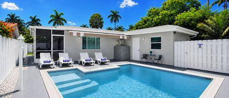 Une piscine avec des chaises longues, un patio couvert et une clôture blanche.